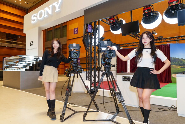 KOBA 2025 소니코리아 부스에서 방송용 카메라 앞에 포즈를 취하고 있는 모델들. 후면에는 조명과 촬영 장비가 배치되어 있는 시연 공간이 보인다.