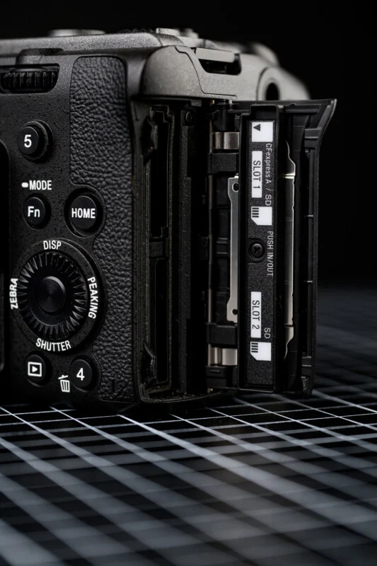Sony FX2의 메모리 카드 슬롯 부분을 클로즈업으로 촬영한 이미지. CFexpress Type A 겸용 슬롯 1번과 UHS-II SD 슬롯 2번이 뚜껑을 연 상태로 노출되어 있으며, 바디 측면에는 다양한 물리 버튼과 다이얼이 배치되어 있다.