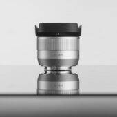 TTArtisan AF 35mm F1.8 II 실버 렌즈가 반사되는 표면 위에 세워져 있는 모습, 블랙 후드를 장착한 정면 이미지