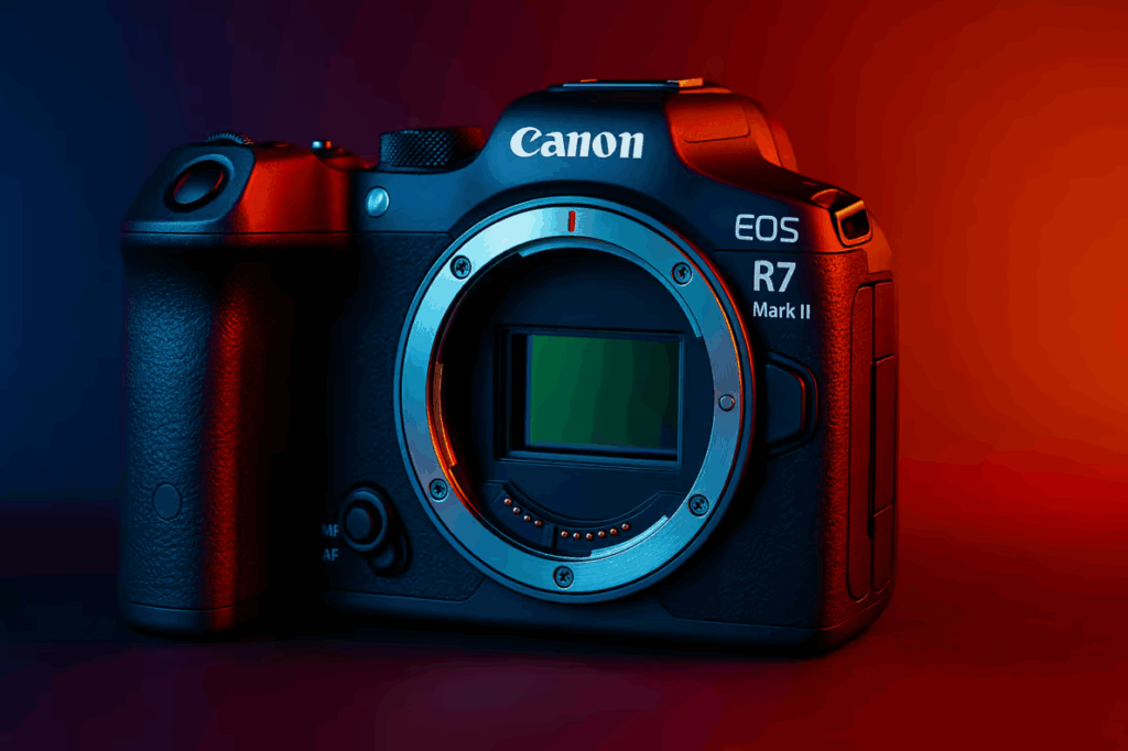 Canon EOS R7 Mark II 카메라가 파란색과 붉은색 조명이 교차되는 분위기 있는 조명 아래에서 강조되고 있으며, 렌즈 마운트가 노출된 상태로 센서와 디테일한 표면 텍스처가 선명하게 표현되어 있다.