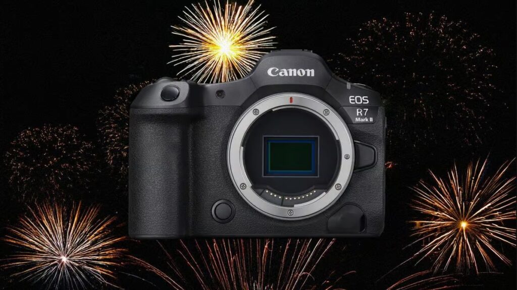 Canon EOS R7 Mark II 미러리스 카메라가 화려한 폭죽 배경 위에 전면 센서 노출 상태로 놓여 있다. 검은 배경에 다양한 색상의 불꽃놀이가 번쩍이며 신제품 발표의 분위기를 강조한다.
