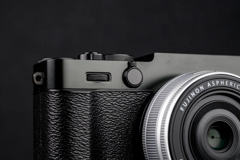 Fujifilm X-E5 카메라의 상단 왼쪽 커맨드 레버와 텍스처 그립 부분 클로즈업, 조작성 강조