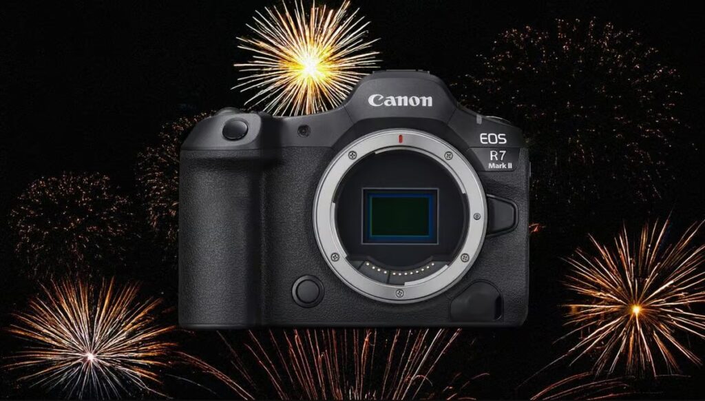 불꽃놀이 배경 위에 놓인 캐논 EOS R7 Mark II 카메라. 렌즈가 장착되지 않은 상태로 센서가 드러나 있으며, 기계식 셔터가 제거된 콘셉트를 시사하는 구성이다.