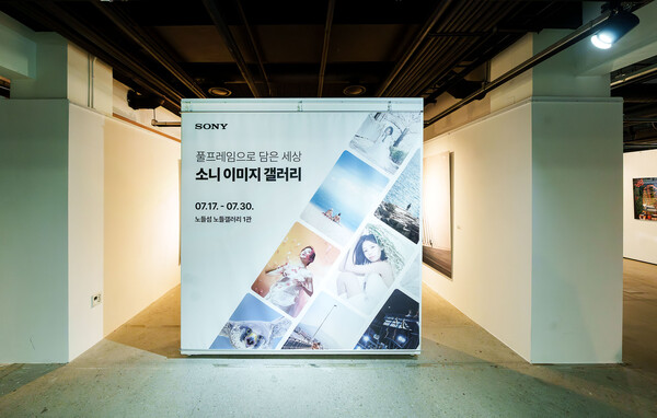 소니 이미지 갤러리 '풀프레임으로 담은 세상' 전시 입구 배너. 흰색 바탕에 'SONY' 로고와 함께 전시 제목, 기간(07.17 - 07.30), 장소(노들섬 노들갤러리 1관) 정보가 적혀 있고, 풀프레임 카메라로 촬영한 다양한 사진들의 콜라주 이미지가 배치되어 있다. 배너는 전시 공간 입구 중앙에 세워져 있으며, 양 옆으로는 다른 전시 공간으로 이어지는 통로가 보인다.