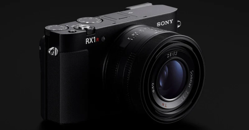 약간 오른쪽 측면에서 촬영된 소니 RX1R III 카메라의 모습입니다. 렌즈와 "SONY", "RX1R III" 로고가 여전히 잘 보이며, 카메라 상단의 다이얼과 버튼 일부가 드러나 있습니다.