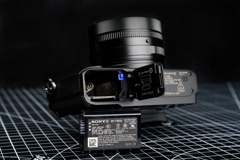 Sony RX1R III의 배터리 슬롯과 NP-FW50 배터리, 하단부 오픈된 상태로 배치된 제품