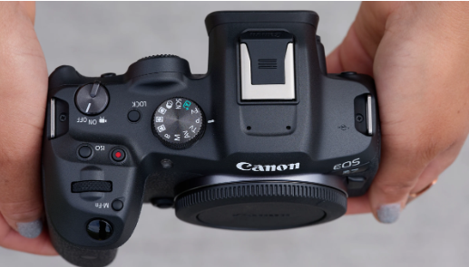 Canon EOS 카메라 상단부를 두 손으로 잡은 모습 – 모드 다이얼, 전원 스위치, 핫슈 단자, 셔터 버튼이 보이는 클로즈업