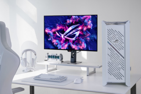 화이트 톤 게이밍 데스크 세팅에 배치된 ASUS ROG 게이밍 모니터와 데스크탑 본체. 모니터 화면에는 ROG 로고가 화려한 컬러 그래픽으로 표시되어 있으며, 헤드셋과 기계식 키보드 등 주변 장비가 함께 놓여 있다.