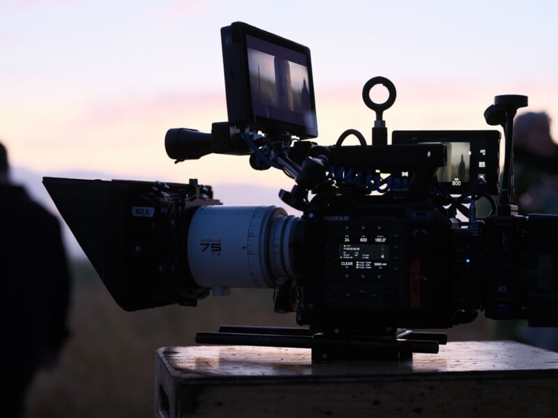 Fujifilm GFX Eterna 55 cinema camera rig with a 75mm cinema lens and external monitors, positioned on a wooden box outdoors during sunset filming.