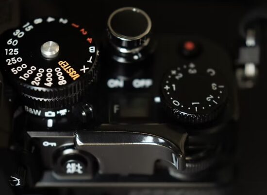 니콘 Zf 카메라 상단 셔터 속도 다이얼과 보조 다이얼 옆에 부착된 Kamerakraft 엄지받침대 클로즈업, 블랙 코팅 마감이 반짝이는 모습