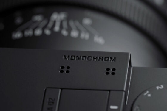 Leica Q 시리즈 모노크롬 카메라 상단부 클로즈업 – 블랙 바디에 ‘MONOCHROM’ 각인이 새겨져 있으며 조작 다이얼과 렌즈 눈금이 일부 보이는 모습