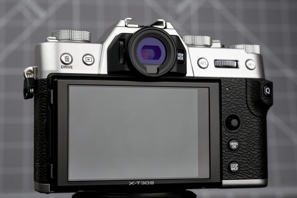 후지필름 X-T30 III 카메라 후면 디자인. 틸트형 LCD 화면과 아날로그 스타일 다이얼, 드라이브 버튼, AEL/AFL 버튼 등이 보인다.