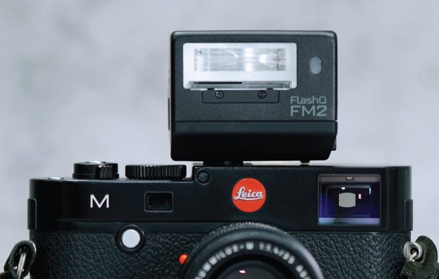 라이카 M 카메라 위에 장착된 블랙 컬러의 LightPix Labs FlashQ FM2 플래시. 심플하고 직각형 디자인의 플래시가 클래식한 레인지파인더 스타일 바디와 자연스럽게 어우러진 모습이다.