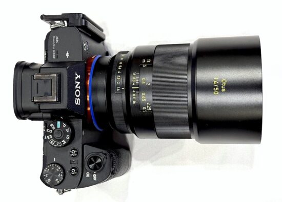 Sony 미러리스 카메라에 Zeiss Otus 50mm f/1.4 렌즈가 장착된 모습. 검은색 금속 하우징의 렌즈가 장착되어 있으며, 상단에서 본 뷰로 Zeiss 특유의 파란 마운트 링과 조리개 눈금이 보인다.