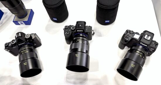 Nikon, Sony, Canon 카메라에 각각 Zeiss Otus 렌즈가 장착된 모습. 세 대의 카메라가 테이블 위에 나란히 놓여 있으며, 각 바디에는 검은색 Otus 1.4 렌즈가 장착되어 있다. 뒤쪽에는 Zeiss 렌즈 케이스가 함께 전시되어 있다.