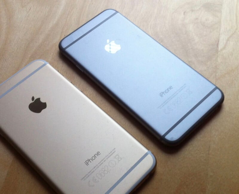 금색과 회색의 아이폰 두 대가 나란히 놓여 있다. 두 제품 모두 후면 카메라가 제거된 ‘NonCam iPhone’ 모델로, 애플 로고와 ‘iPhone’ 문구만 보인다.